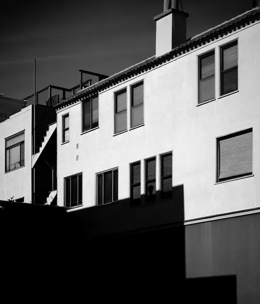 White facades and shuttered windows caught in a dramatic interplay of light and deep shadow, black and white architectural street photography in San Francisco