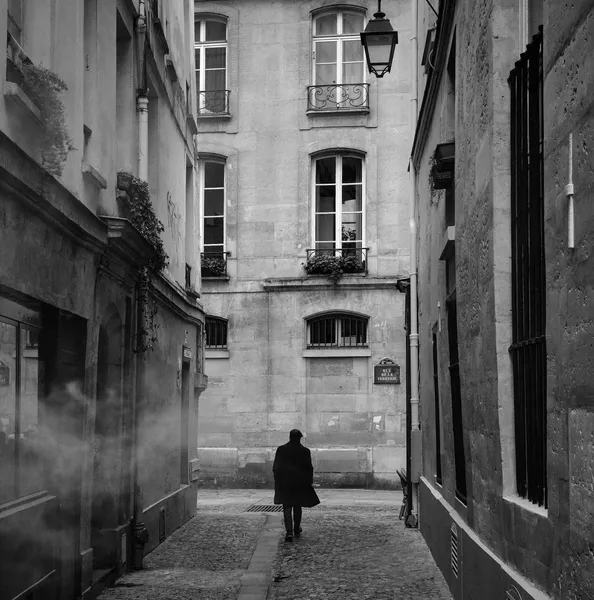 A solitary silhouette walks into a narrow Parisian alley where fog and old lanterns conjure a mysterious, cinematic atmosphere
