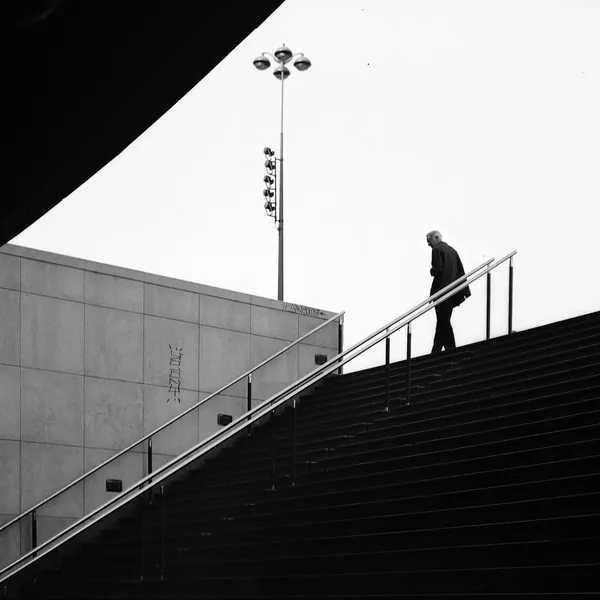 A solitary figure descends a monumental staircase framed by bold diagonal lines and a striking geometric overhang, black and white urban architecture in Paris