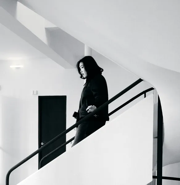A woman descends the iconic staircase of Villa Savoye, her dark silhouette framed by pristine white walls and angular modernist lines