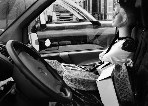 A mannequin seated in a car like a silent passenger, staring out with blank composure through the windshield in Trouville-sur-mer