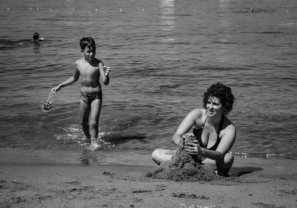 A child dashes through the shallows while a woman builds a sandcastle on the Croatian shore, a tender moment of summer joy on Kolocep island