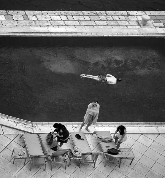 Aerial view of a swimming pool in Dubrovnik where a figure floats alone while others lounge poolside, an overhead study of leisure and solitude