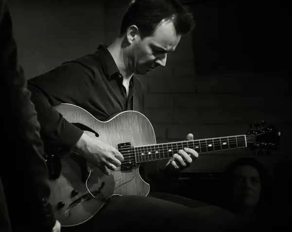 Jazz guitarist Jesse van Ruller lost in concentration during a live performance in Paris, fingers dancing across the strings in warm stage light