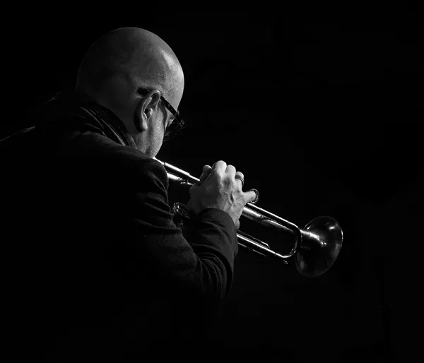 Trumpeter Stéphane Belmondo emerges from deep shadow, the brass instrument gleaming as he plays in this dramatic black and white jazz concert portrait