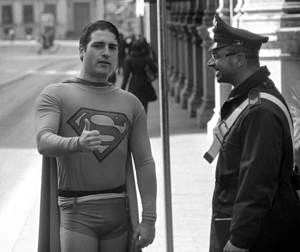 A man dressed as Superman chats with a smiling police officer on a Roman street, a playful encounter between fiction and authority