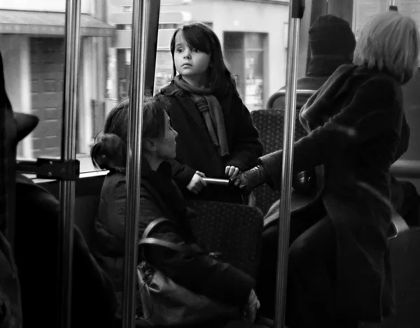 A child gazes upward with wide wondering eyes on a Parisian bus, a candid portrait of innocent curiosity amid the blur of commuters