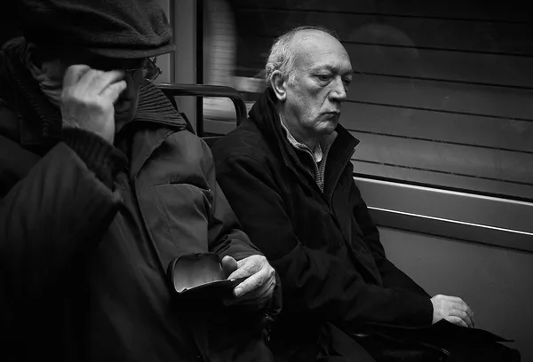 A man sits in the Paris metro with a stern contemplative expression, a portrait of quiet resilience amid the routine of urban commuting
