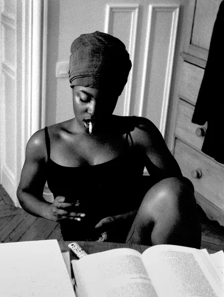 A young woman absorbed in reading, her headwrap and poised silhouette composing a luminous black and white portrait of quiet concentration in Paris