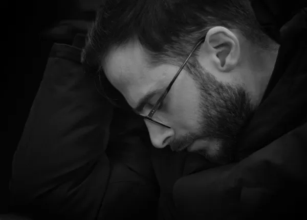 A man curled up and sleeping in the Paris metro, glasses still on, surrendering to exhaustion in a tender close-up portrait