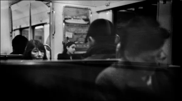 Faces adrift in the blur of a Parisian metro ride, a woman gazes through the crowd as reflections layer over the windows like passing thoughts
