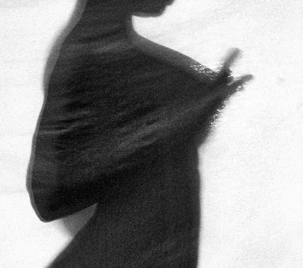 A blurred silhouette of a figure rendered like a brushstroke on paper, grain and motion dissolving identity into pure graphic form