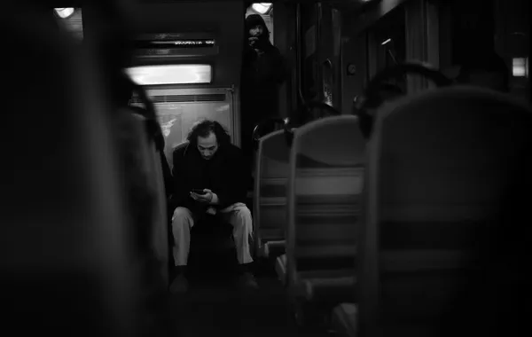 A lone passenger hunches over his phone at the far end of an empty Parisian metro car, swallowed by the dim glow of the carriage