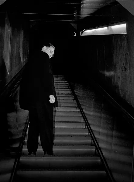 A figure ascends a dark metro staircase toward a single fluorescent light, a modern Orpheus climbing out of the underground depths of Paris