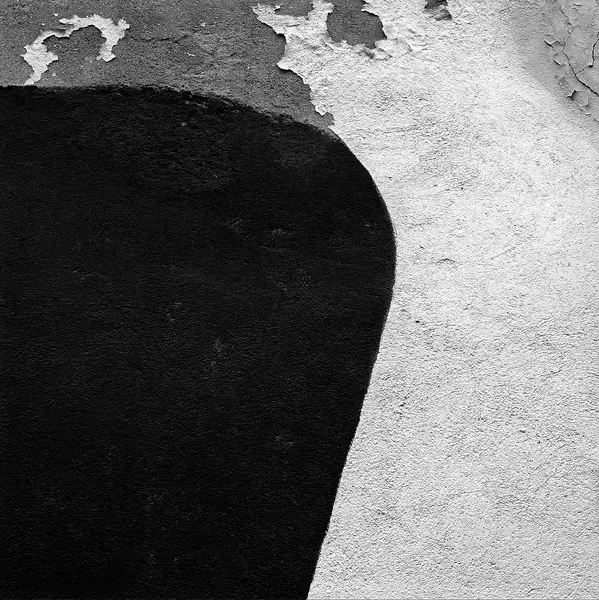 A bold abstract composition of peeling paint on a wall in Sète, a stark black curve meeting rough white plaster like a minimalist painting found in the street