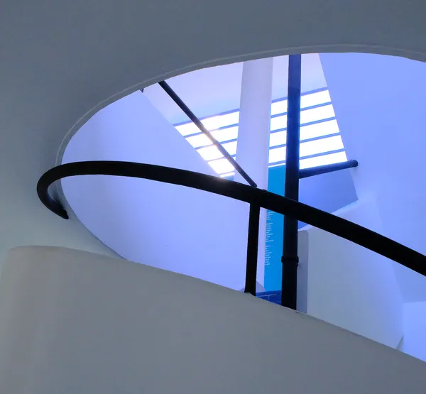 The spiral ramp of Villa Savoye bathed in ethereal blue light, black railing sweeping upward toward a skylight in this color study of modernist architecture