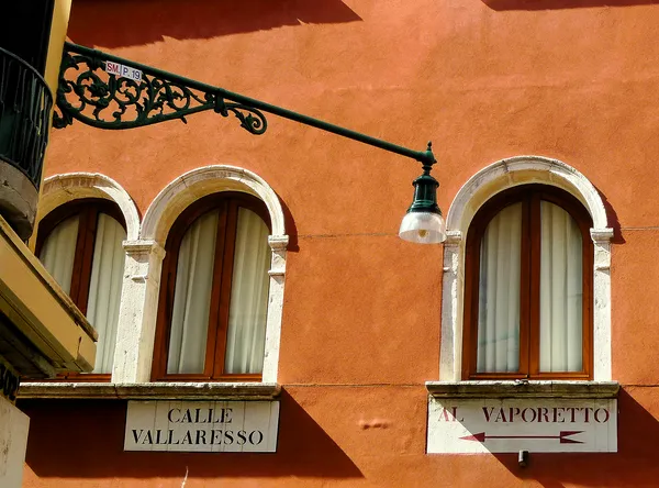Warm terracotta facade of a Venetian building on Calle Vallaresso, arched windows and an ornate iron street lamp bathed in golden Mediterranean light