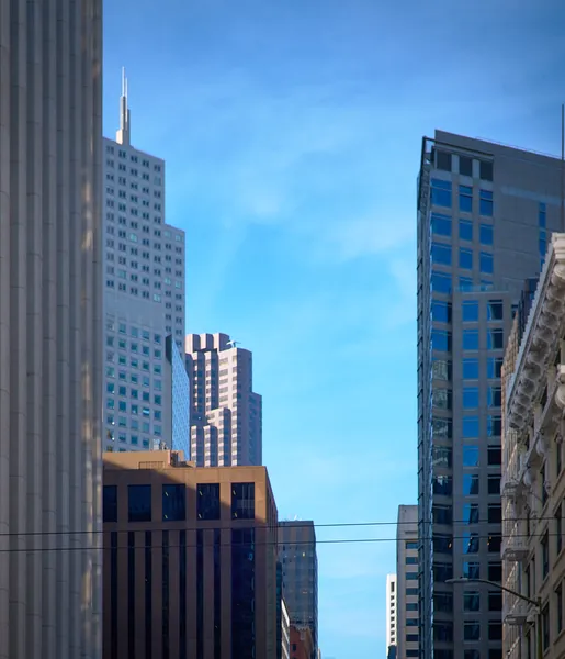San Francisco skyscrapers crowd together against a clear blue sky, their varying facades creating a dense vertical mosaic of glass and stone
