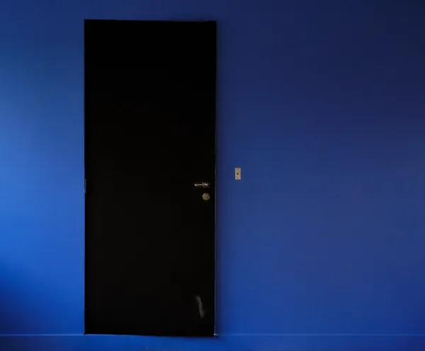 A black door stands in a saturated deep blue wall, a mysterious minimalist composition evoking the cinematic universe of David Lynch in Poissy