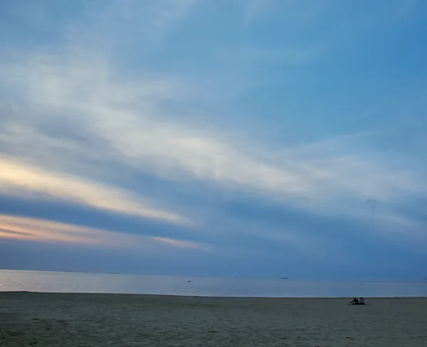 A vast beach at twilight in Trouville-sur-mer, a lone figure tiny beneath an immense sky streaked with soft blue and golden clouds