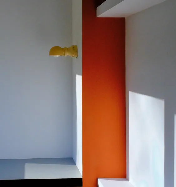 A bold orange wall meets soft grey surfaces inside Villa Savoye, natural light carving geometric color fields in Le Corbusier's modernist palette